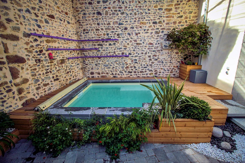 Une mini piscine, du bois, de la pierre et des végétaux. Piscine équipée d'une pompe à chaleur, d'une couverture à barres